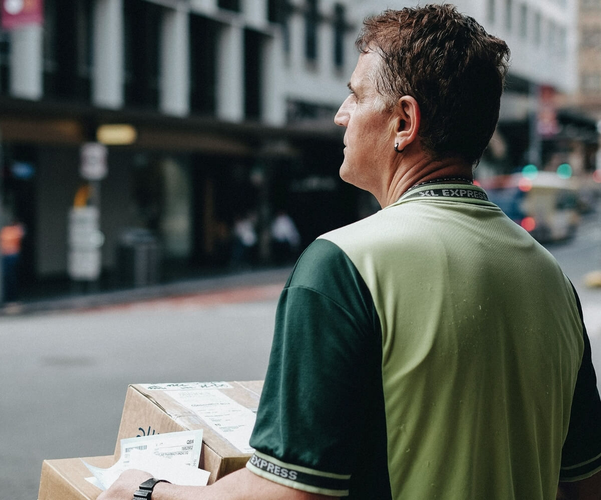 Livreur en veste verte portant un colis en ville